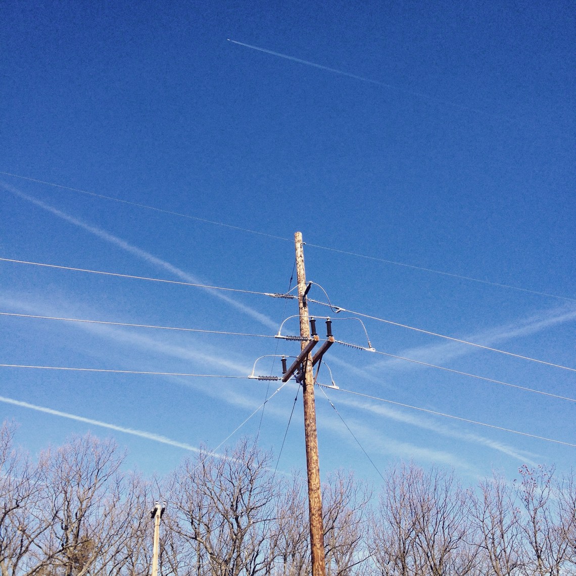 Powerline against a sky crossed by multiple contrails.