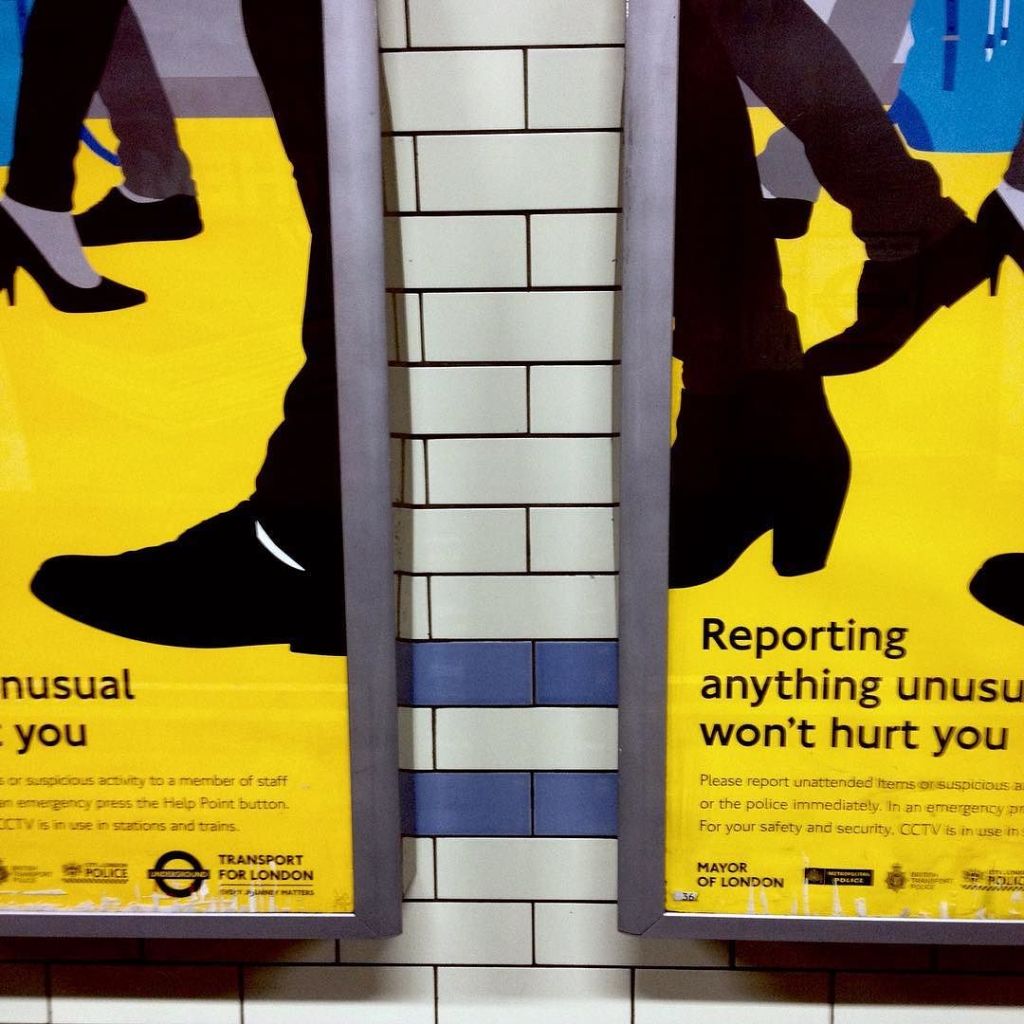 Two identical signs, with a gap between them, showing a graphic of walking feet and urging people to report anything unusual.